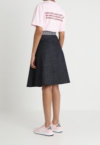 T-shirt rosa con scritte rosse, gonna di jeans scuro, e sneakers rosa chiaro con strisce nere. La gonna è a trapezio, arriva al ginocchio ed è aderente in vita.