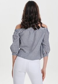 Striped off-the-shoulder blouse in navy and white, featuring three-quarter sleeves and a loose fit, paired with white denim jeans.