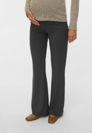 Person wearing dark gray wide-leg pants, a beige ribbed sweater, and brown square-toe shoes, standing against a plain background.