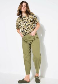 Top de manga corta con estampado de leopardo en beige y negro; pantalones verdes oliva ajustados; zapatos de ante suaves tipo slip-on con adornos decorativos.