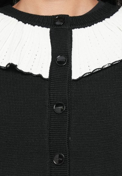 Cardigan nero lavorato a maglia con un colletto bianco a coste con bordi ondulati, arricchito con bottoni neri sul davanti.