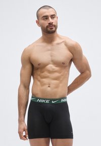 Boxeri negri Nike cu o talie verde pe care este afișat logo-ul Nike. Țesătura pare moale, cu o textură netedă.