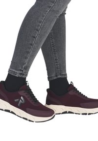 Bordeaux rote Mesh-Sneaker mit schwarzen Akzenten, weißer Sohle und einem gemusterten Gummi-Profil. Tragen mit dunkelgrauen Skinny-Jeans.