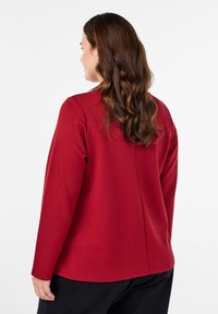 Crvena majica dugih rukava s glatkom teksturom, okruglim izrezom i ravnim krojem, s diskretnim šavom na leđima.