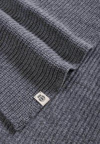 Knitted grey scarf featuring a textured pattern with alternating ribbed and flat sections. Includes a small fabric label at one corner.