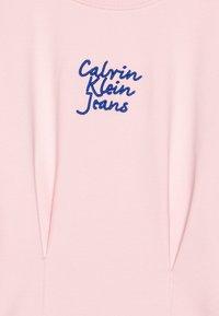 Camisa de algodão rosa com um logotipo bordado em azul "Calvin Klein Jeans" na parte da frente. Textura suave e design simples, decote redondo.