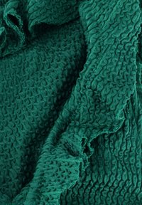 Textured fabric in dark green with a wave pattern, featuring pleated and crinkled sections, creating a layered appearance.