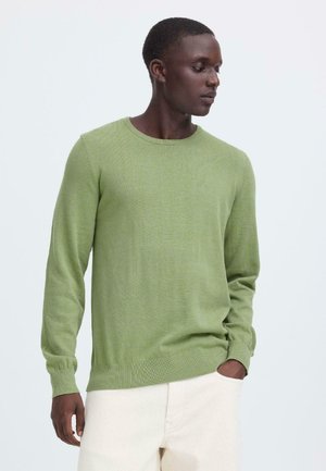 Groene gebreide trui met lange mouwen en een ronde hals, met een gladde textuur en geribbelde manchetten, gecombineerd met lichtgekleurde broek.