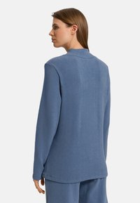 Top in cotone blu misto con vestibilità rilassata, maniche lunghe e una sottile trama. Presenta un colletto casual e un orlo allungato.