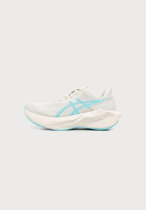 Chaussure de course gris clair avec une semelle épaisse texturée et un logo bleu clair ainsi que des accents sur la semelle, présentée en profil latéral sur un fond uni.