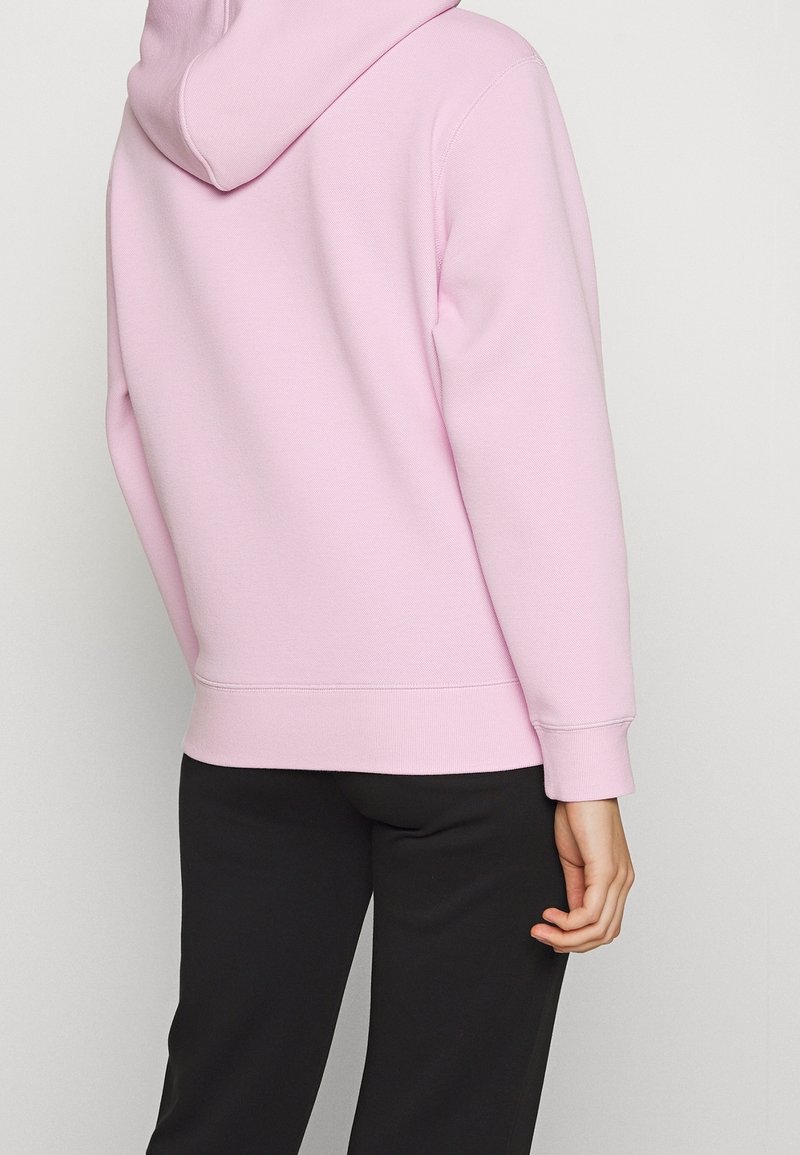 Sudadera con capucha rosa en una mezcla suave de algodón, con un corte relajado, puños y dobladillo acanalados, combinada con pantalones negros.