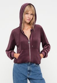 Fluwelen rits hoodie in diep paars met een voorzak, verstelbare trekkoordcapuchon en geribde cuffs.