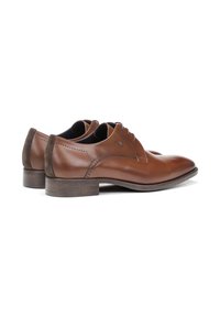 Zapatos de vestir de cuero marrón con textura suave, punta redondeada, costuras sutiles y un tacón bajo de madera apilada. Detalles en ante oscuro en el talón.