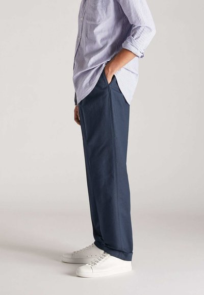 Pantalones azul marino de corte recto, con bolsillos laterales. Combinados con una camisa de rayas de botones y zapatillas blancas.