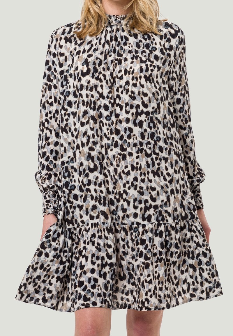 Femme portant une robe longue à imprimé léopard avec des manches longues et des poignets froncés, tenant légèrement l'ourlet d'un côté.