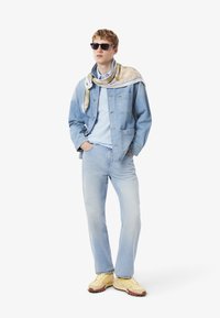 Vaaleansininen farkkutakki, siihen sopivat farkut, vaaleansininen toppi, kuviollinen huivi ja keltaiset lenkkikengät ruskeilla yksityiskohdilla. Aurinkolasit täydentävät asun.