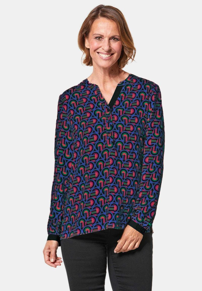 Langsleeve blouse van levendig zwart stof met een kleurrijk geometrisch patroon in roze, blauw en groen; V-hals ontwerp en manchetten.