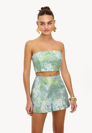 Crop top sans manches et short assorti en tissu léger et brillant bleu clair avec des motifs floraux verts et une texture lisse.