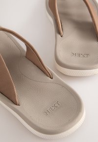 Braune Flip-Flops mit glatten Gummisohlen und strukturierten Innensohlen. Ausgestattet mit schlanken Riemen in Rippendesign. "NEXT"-Logo ist in die Sohle geprägt.