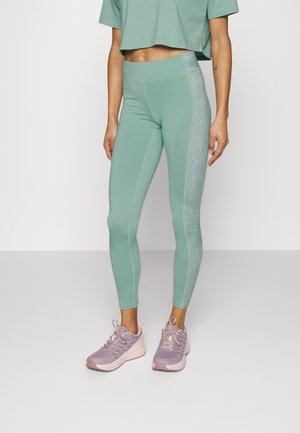 Leggings vert menthe avec un panneau latéral texturé, design ajusté et couture contrastée. Assortis avec des chaussures de sport violettes claires.
