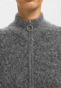 Grå zip-up tröja gjord av mjukt, texturerat material. Har en hög krage och en metallisk dragkedja med en rund dragring.