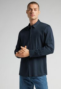 Marineblauw overhemd met lange mouwen, knoopsluiting en kraag, met een gladde textuur en een voorste sluiting, gecombineerd met blauwe denim jeans.