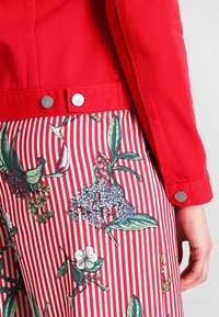 Röd denimjacka med silverknappar, lager på lager över randig tyg med blommönster i gröna, blå och vita nyanser.