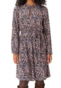 Femme portant une robe à fleurs à manches longues avec une taille cintrée et un décolleté en trou de serrure, associée à des bottes marron montantes.