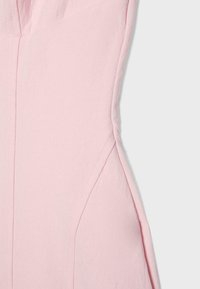 Tissu rose clair avec des lignes de couture visibles et des surpiqûres, montrant un gros plan des détails de la confection du vêtement.