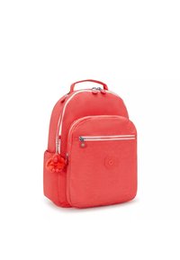 Mochila coral con un acabado de tela suave, compartimentos con doble cremallera, bolsillo lateral y un llavero decorativo de mono. Detalle del logo circular.