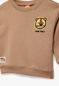 Brązowy sweatshirt z okrągłym dekoltem, z haftem w kształcie twarzy lwa oraz napisem "ROAR VIBES" poniżej. Miękka, teksturowana tkanina.