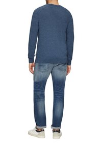 Niebieski sweter z teksturą i długimi rękawami; zestawiony z wyblakłymi niebieskimi dżinsami z podwiniętymi nogawkami oraz białymi trampkami z ciemnymi akcentami.