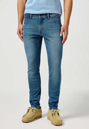 Jeans in denim blu, taglio slim, con un classico design a cinque tasche e una leggera sfumatura. Indossati con scarpe in suede beige.