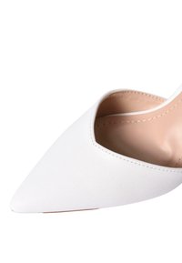 Scarpa con tacco alto in pelle bianca, con punta affilata, design a forma di V e cuciture minimaliste. L'interno presenta una fodera liscia nude.