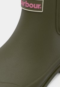 Γόνατο από καουτσούκ σε σκούρο ελιά χρώμα με υφή, με ροζ και λευκό λογότυπο Barbour στο πάνω μέρος. Στρογγυλεμένος σχεδιασμός με χαμηλό τακούνι.