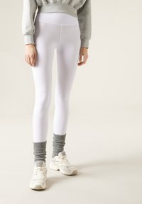 Leggings bianchi realizzati in materiale elastico, abbinati a calzini grigi arricciati e sneaker bianche testurizzate. Design e vestibilità semplici.