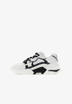 Weißer und schwarzer Sportschuh mit klobiger Sohle, schwarzen Schnürsenkeln und "GUESS"-Logo an der Seitenplatte.