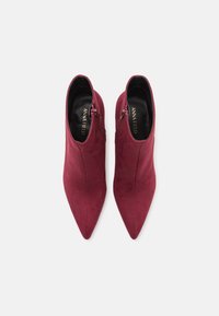 Botines burdeos de ante con punta afilada y cremalleras laterales, que cuentan con una textura suave y una silueta elegante.