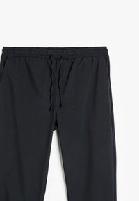 Svarta joggarbyxor med elastiskt midjeband, justerbar dragsko och en slät, matt yta. Har sidofickor.