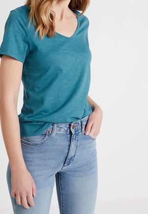 Tealfarbenes T-Shirt mit kurzen Ärmeln und V-Ausschnitt aus weichem Stoff, kombiniert mit hellblauen, hoch taillierten Jeans mit klassischem Knopf- und Reißverschluss.