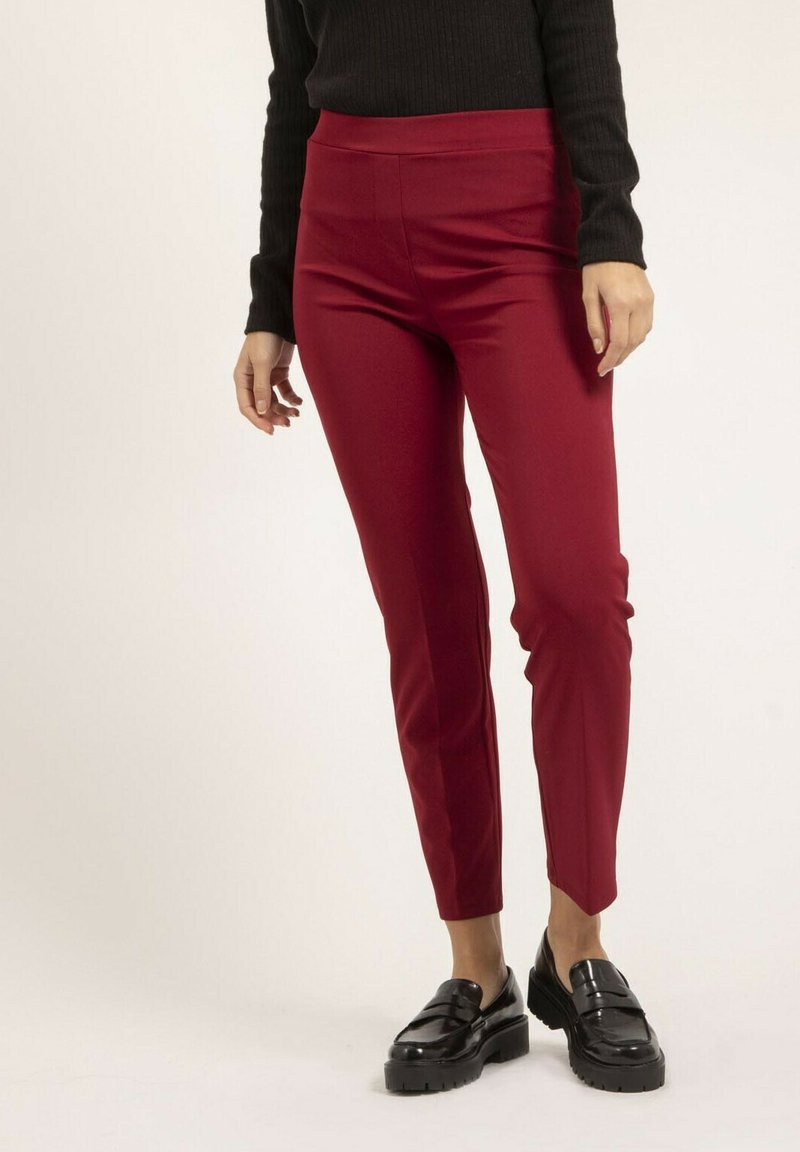 Pantalons ajustés rouge à taille haute, texture lisse, design slim et coupe au niveau de la cheville. Accompagnés de chaussures à plateforme noires.