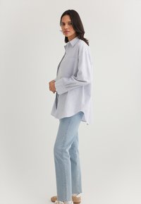 Blue and white striped button-up shirt with a relaxed fit, paired with light blue denim jeans and casual white sneakers.