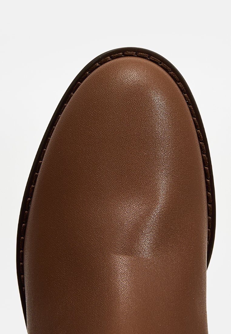 Bottines en cuir marron avec une texture lisse, bout arrondi et piqûres contrastantes le long du bord. Pas d'ornements notables.
