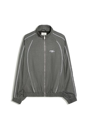 Veste grise zippée avec de fines rayures verticales blanches, poignets et ourlet élastiques, et passepoil blanc le long des manches et des côtés avant.