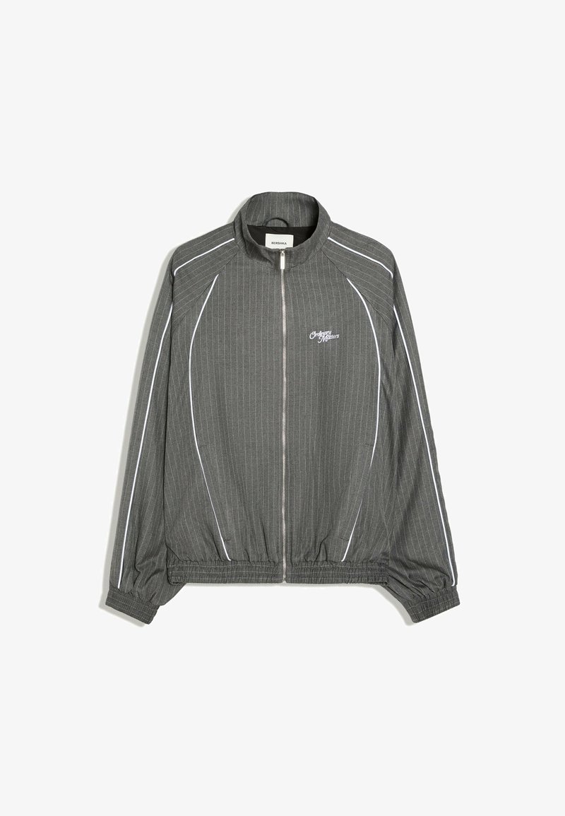Veste grise zippée avec de fines rayures verticales blanches, poignets et ourlet élastiques, et passepoil blanc le long des manches et des côtés avant.