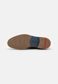 Suela de zapato de cuero marrón con un patrón de agarre de goma, presenta una entresuela azul y un acento rojo en el talón. Superficie texturada para tracción.