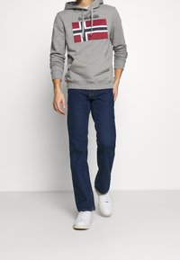 Sudadera gris con un gráfico de la bandera noruega de rayas rojas y marinas, combinada con jeans azules y zapatillas blancas. Ajuste casual, material de algodón.