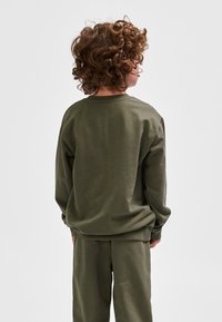 Olijfgroene trui gemaakt van zachte stof met een ontspannen pasvorm. Voorzien van een ronde hals en geribbelde manchetten, gecombineerd met een bijpassende broek.