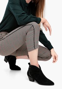 Svarta mocka ankelstövlar med spetsig tå och medelhög blockklack, bärs tillsammans med mönstrade, korta byxor med rutmönster i beige och röd.