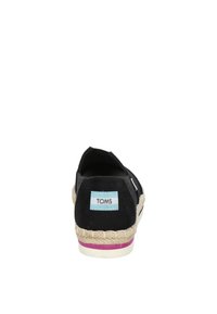 Zwarte canvas espadrille met gevlochten jute zool en roze accent. Kenmerkt zich door de stiksels langs de zijkanten en het prominente "TOMS" logo op de hiel.